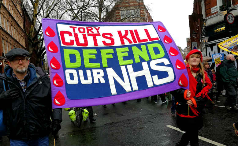 A brightly coloured banner on the Fund Our NHS march on Saturday 3rd February, reading 'Tory cuts kill ; Defend our NHS'