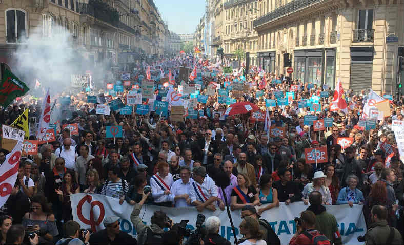 La France Insoumise leaders at the head of a massive marching crowd stretching back right into the distance of a Paris boulevard, with 