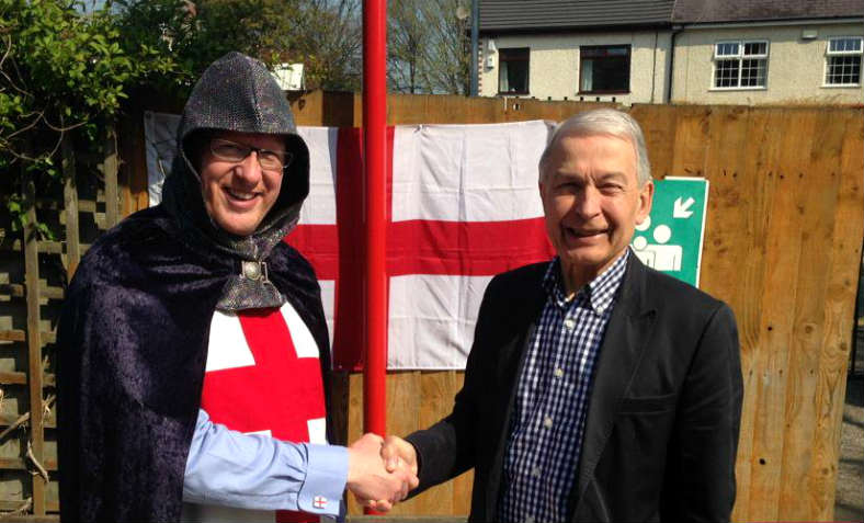 Frank Field MP stands smiling and shaking hands with a man dressed as St George - celebrating St George's day at a school in his Birkenhead constituency in 2015.