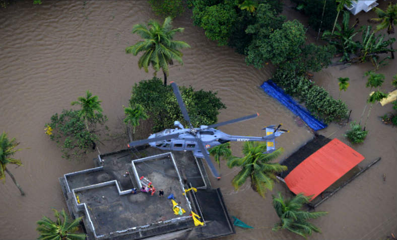 Indian Southern Naval Command helicopter hovers over a building amidst the flood in Kerala - people are being rescued below.