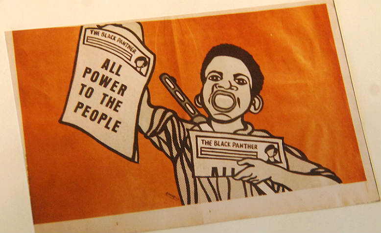 An iconic image from the Black Panther Party newspaper, with a young man waving copies of their newspaper, shouting (mouth open) and with an automatic rifle strapped to his back.