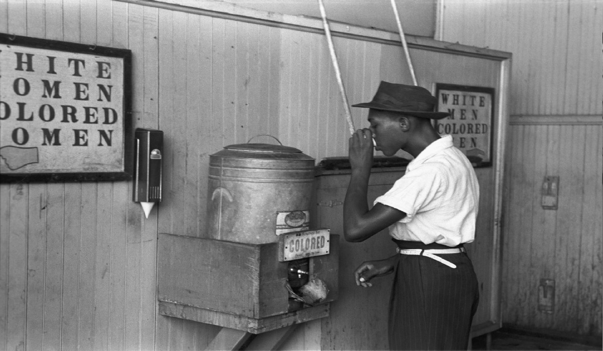 Image of an African-American man drinking from a segregated water fountain.