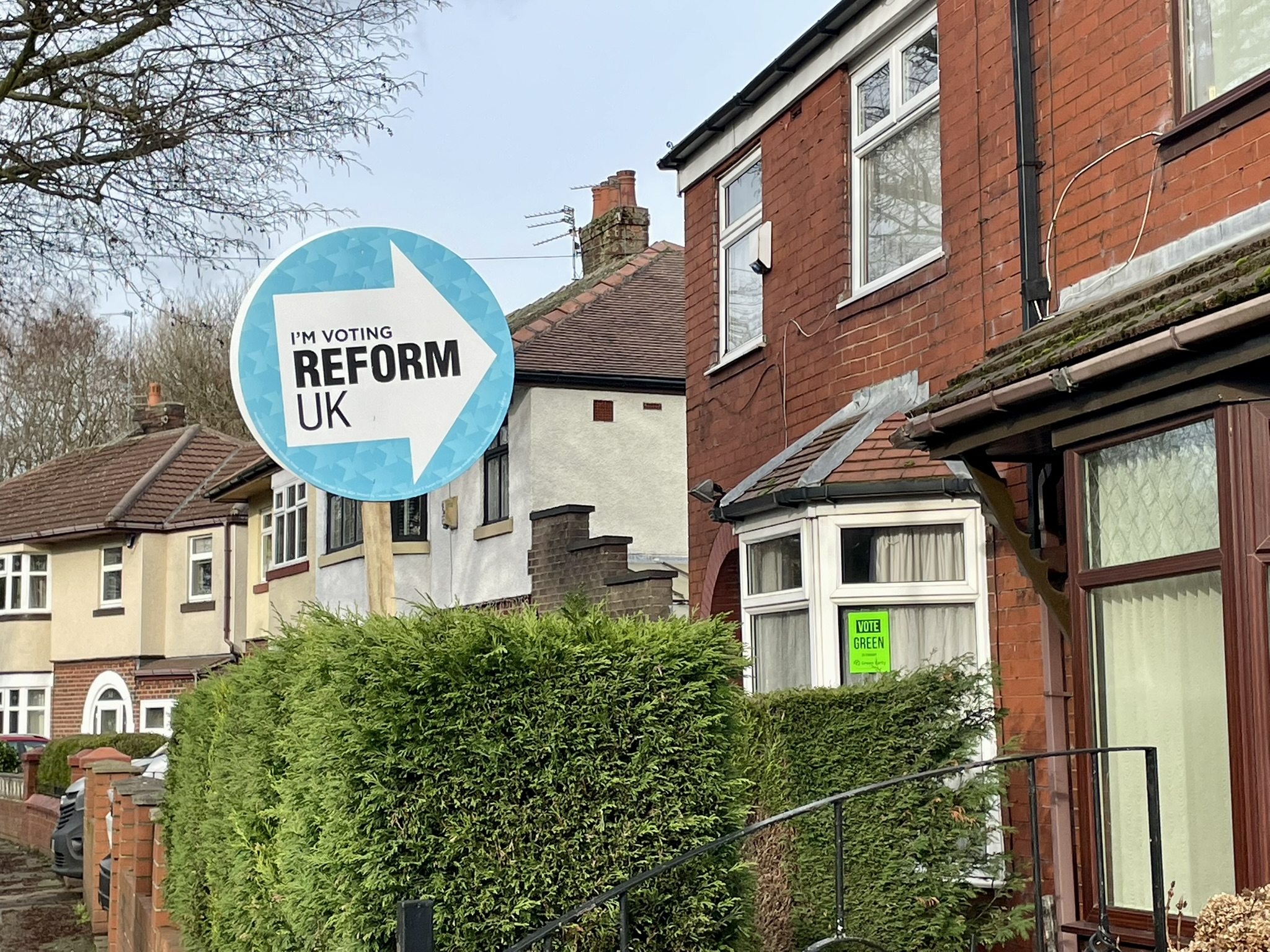 Posters for Reform and the Green Party outside adjacent houses in Denton, Greater Manchester.